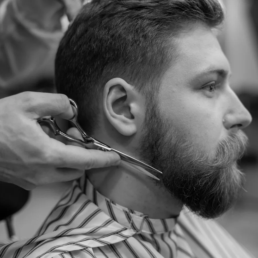 Barbeiro aparando a barba de um cliente com tesoura.